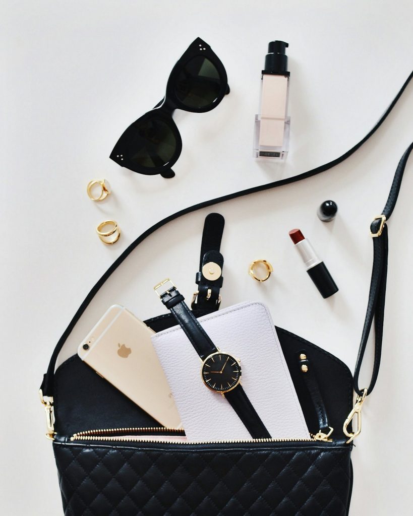 Home Assorted stylish accessories including a handbag, sunglasses, perfume, watch and smartphone laid out on a white surface